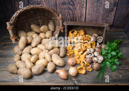 Patate, funghi, prezzemolo, erba cipollina e cipolle su un tavolo di legno Foto Stock