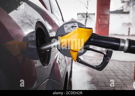 La pistola di riempimento gialla viene inserita nel foro del serbatoio del gas dell'auto durante il rifornimento di benzina. Primo piano della pistola a carburante. Lo sfondo è sfocato Foto Stock