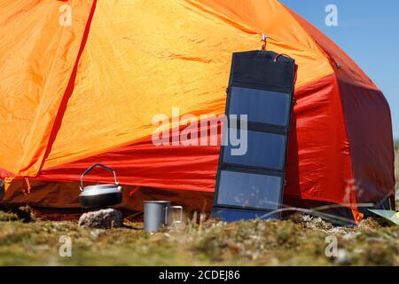 Pannello turistico solare su tenda arancione in esterno. Attrezzature da campeggio, energia di fonte alternativa. Foto Stock