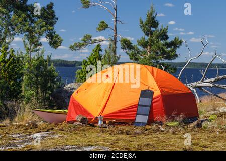 Tenda arancione, pannello solare turistico, kayak di mare, macchina per il caffè sull'isola. Attrezzature da campeggio, attività all'aperto, kayak Foto Stock