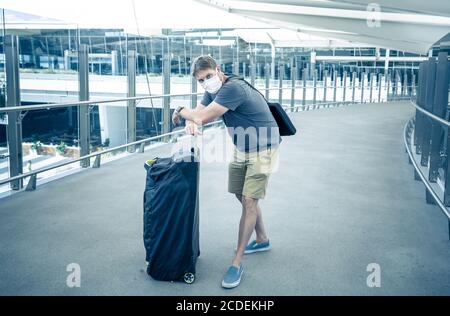 COVID-19 viaggia nella nuova normalità. Viaggiatore con maschera protettiva al terminal dell'aeroporto preoccupato di quarantena di ritorno a casa. Passeggero bloccato in airpo Foto Stock