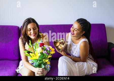 Adorabile giovane ragazza sorprende la mamma con bouquet di fiori e biscotti. Buon giorno della mamma o compleanno. Concetto di celebrazione familiare. Foto Stock