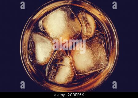 Un bicchiere di cola con un primo piano di ghiaccio al buio. Bevanda gassata marrone, bevanda analcolica con caffeina. Vista dall'alto Foto Stock
