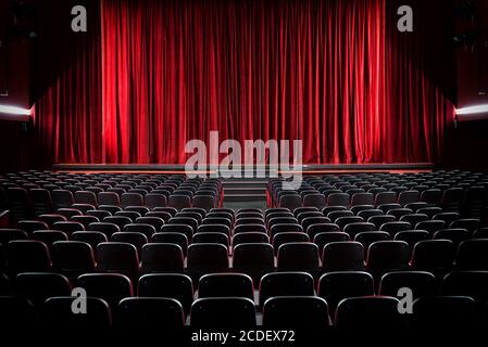 Oscurato cinema vuoto e palcoscenico con le tende rosse vista su file di sedili vuoti dalla parte posteriore Foto Stock