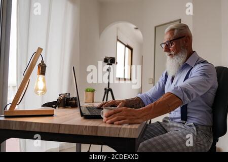 Immagine ritagliata di un uomo anziano che lavora sul suo laptop in uno studio, vista posteriore delle mani di un uomo d'affari occupato utilizzando il computer portatile alla scrivania dell'ufficio. Foto Stock