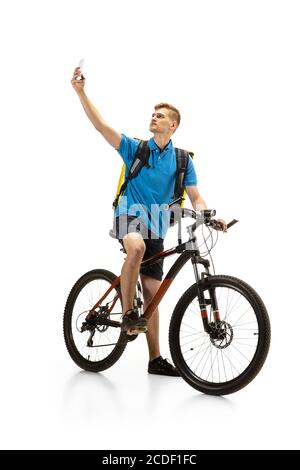 Presa selfie. Deliveryman con bicicletta isolata su sfondo bianco studio. Servizio senza contatto durante la quarantena. L'uomo consegna il cibo durante l'isolamento. Sicurezza. Occupazione professionale. CopySpace per l'annuncio. Foto Stock