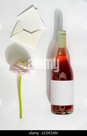 Cartolina di congratulazioni con bottiglia di vino rosato, fiore naturale tenero e cartolina di lettera in una busta su uno sfondo grigio chiaro con ombre, copia s. Foto Stock
