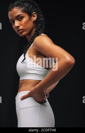 Vista laterale ritratto di sportivo in abbigliamento da fitness bianco. Primo piano di atleta femminile in piedi su sfondo nero. Foto Stock