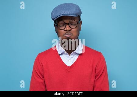 Giovane bell'uomo africano che soffica le guance con il viso divertente che trattiene il respiro. Foto Stock