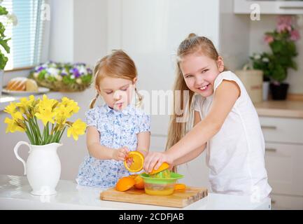 Due bambini con centrifuga e arance fanno succo d'arancia fresco in cucina Foto Stock