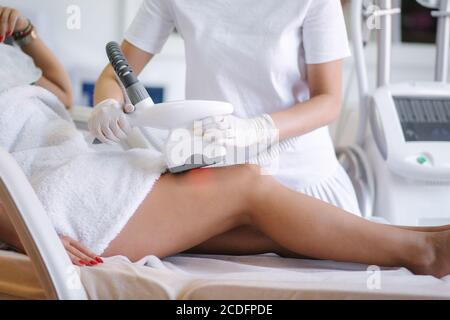 Donna attraente ha un riposo mentre cosmetologist in guanti bianchi che eseguono la procedura di sollevamento a radiofrequenza sullo stomaco. Bella donna dentro Foto Stock