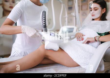 Donna attraente ha un riposo mentre cosmetologist in guanti bianchi che eseguono la procedura di sollevamento a radiofrequenza sullo stomaco. Bella donna dentro Foto Stock