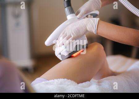 Dermatologo professionista in guanti bianchi che esegue la procedura di sollevamento a radiofrequenza sullo stomaco di una donna. Bella donna in clinica medica Foto Stock