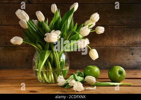 Tulipani bianchi in vaso di vetro su legno rustico Foto Stock