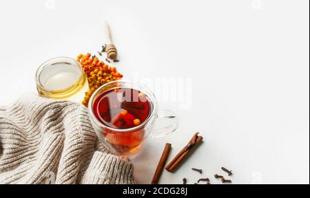 Tè vitaminico con frutti di bosco, miele, Rowan e frutti di mare, bastoncini di cannella e chiodi di garofano secchi su tavolo leggero con pullover in maglia beige. Utile pro Foto Stock