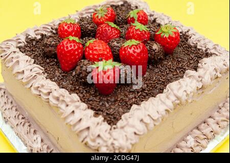Deliziosa torta al cioccolato brasiliana tradizionale chiamata Bolo de Brigadeiro con condimento di fragole fresche. Isolato su sfondo giallo. Primo piano. Foto Stock