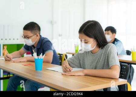 Gruppo di studenti delle scuole elementari asiatiche che indossano una maschera igienica in classe e sorridono per essere felici mentre tornano a scuola riaprono la loro scuola, New Nor Foto Stock