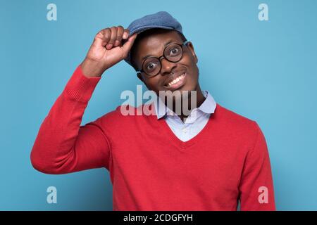 Allegro giovane uomo africano saluta togliendo un cappello Foto Stock