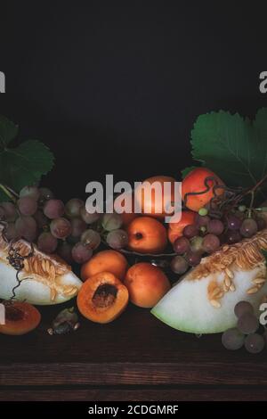 Autunno ancora vita con albicocche, uva e melone, umore scuro Foto Stock