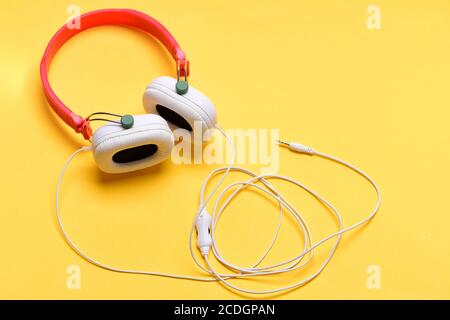 Cuffie per la musica in plastica. Cuffie di colore bianco e rosso con cavo  lungo. Auricolari moderni ed eleganti isolati su caldo sfondo giallo.  Accessori musicali e concetto tecnologico Foto stock -
