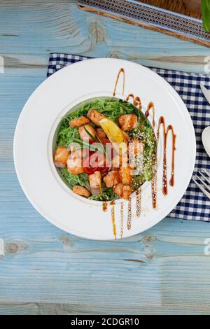 Tagliatelle di riso con salmone e spinaci. Pranzo in un piatto bianco sul tavolo. Pomodori, limone, pesce, rosmarino, semi di soi e sesamo. Cibo ancora vita Foto Stock