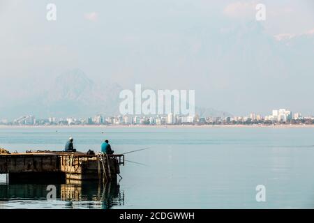 Antalya, Turchia - 22 Febbraio 2019: due pescatori pesca vicino al faro del porto della città vecchia di Kaleici ad Antalya. Foto Stock