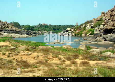 Nella distanza tra l'ambiente arido e il paesaggio roccioso del fiume Tungabhadra, si può vedere il famoso Tempio Birupaksha di Hampi. Foto Stock