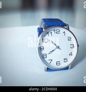 Orologio da polso con cintura blu isolata su pavimento bianco. Foto Stock