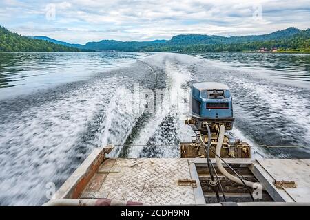 vista del motore sull'imbarcazione a motore da dietro e il sentiero acquatico con spruzzi e paesaggi sul grande lago Foto Stock