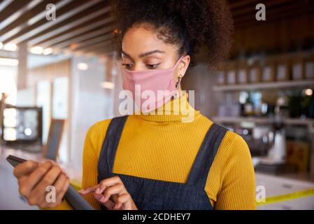 Il proprietario di una caffetteria africana che indossa una maschera facciale davanti al banco che esegue il controllo delle scorte. Foto Stock