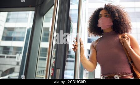 Giovane donna adulta che entra in ufficio indossando la maschera che guarda fuori fotocamera