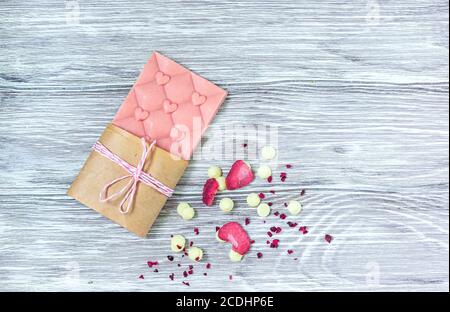 Barretta di cioccolato rosa decorata con fette di frutta a guscio e fette su sfondo grigio. Cioccolato artigianale alla moda. Idea regalo. Foto Stock