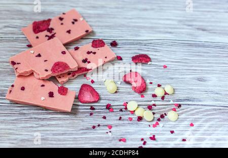 Barretta di cioccolato rosa decorata con fette di frutta a guscio e fette su sfondo grigio. Cioccolato artigianale alla moda. Idea regalo. Foto Stock