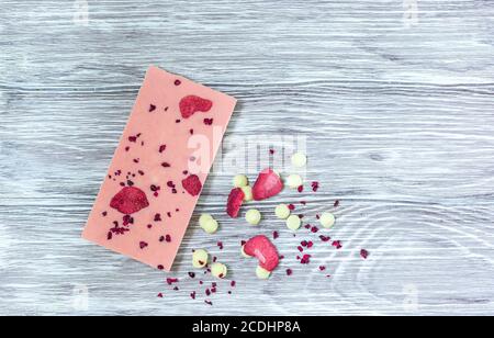 Barretta di cioccolato rosa decorata con fette di frutta a guscio e fette su sfondo grigio. Cioccolato artigianale alla moda. Idea regalo. Foto Stock