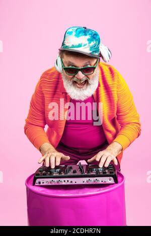 Tempo di festa. Ritratto di uomo hipster anziano in occhiali alla moda isolato su sfondo rosa studio. Concetto di stile di vita per anziani con tecnologia e gioia. Colori alla moda, per sempre giovani. CopySpace per il tuo annuncio. Foto Stock