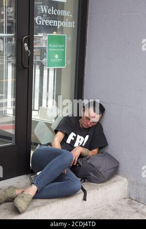 Donna apparentemente è passata fuori all'ingresso di una banca a Greenpoint, Brooklyn con una bottiglia di liquore tra le gambe. Foto Stock