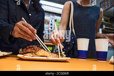 due amici che mangiano pesce al mercato alimentare di strada sono in stallo Kyoto Foto Stock