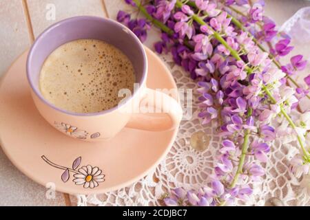 Scena mattutina con una tazza di caffè circondata da selvaggi fiori di lupino Foto Stock