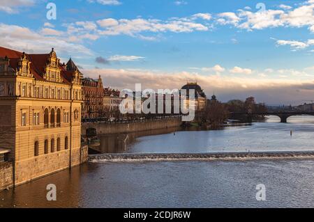 Splendida vista sul lato del fiume Moldava con il Museo Bedřich Smetana, il Teatro Nazionale e il Ponte della Legione dal Ponte Carlo nella soleggiata giornata invernale con il blu Foto Stock