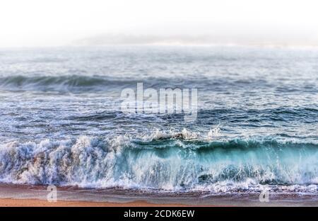 Onde che si schiantano sulla spiaggia con nebbia di sfondo Foto Stock