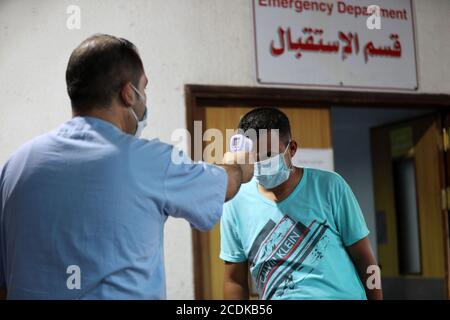 Khan Younis, città della striscia di Gaza di Khan Younis. 28 Agosto 2020. Un operatore sanitario palestinese misura la temperatura corporea di un uomo all'ospedale di al Amal, nella parte meridionale della striscia di Gaza, città di Khan Younis, il 28 agosto 2020. La Palestina ha registrato due morti e 724 nuovi casi COVID-19 nei territori palestinesi nelle ultime 24 ore, annunciato venerdì da un alto funzionario palestinese. Credit: Yasser Qudih/Xinhua/Alamy Live News Foto Stock