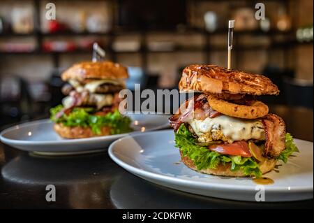 Due hamburger freschi e succosi con manzo, formaggio, pancetta, cipolla e insalata su un tavolo in un caffè. Foto Stock