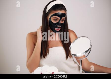 Giovane donna con maschera nera detox di carbonio sul viso, la ragazza adolescente si prende cura della pelle oleosa, pulizia dei pori. Salone di bellezza. Cura della pelle. Foto Stock