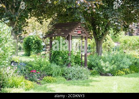 Giardino cortile posteriore con pergolato in legno e piante fiorite con alberi decidui nell'area suburbana Foto Stock
