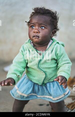 Ranohira, Madagascar - 29 aprile 2019: Bambina malgascia, in abiti strappati, maglione dentro fuori, a malapena in piedi a terra, equilibrando cercando di non Foto Stock