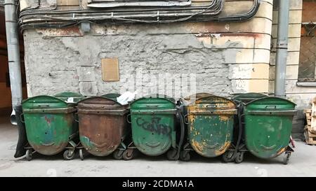 Cinque spazzatura verde sporco, vista frontale, accanto al muro del vecchio edificio. Bidoni della spazzatura chiusi. Concetto di smaltimento dei rifiuti. Vecchi contenitori Foto Stock