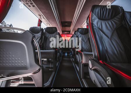 Un interno vuoto di un autobus interurbano regolare con file di sedili in pelle numerati con bordi rossi, corridoio dei sedili in moquette al centro; fuoco selettivo Foto Stock