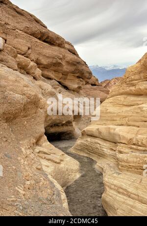 Un canyon stretto con pareti ricche di colori vivaci e stratificate serpeggia verso montagne lontane innevate Foto Stock