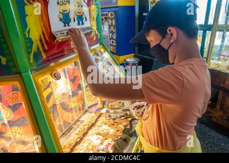 Un ragazzo gioca un penny cade gioco in una galleria di divertimento mentre in vacanza in Devon. Indossa una maschera facciale a causa delle restrizioni del coronavirus. Foto Stock