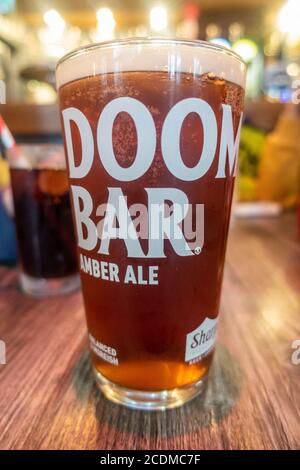 Una pinta di Doom Bar Amber Ale in una pinta di vetro su un tavolo di legno in un pub. Foto Stock